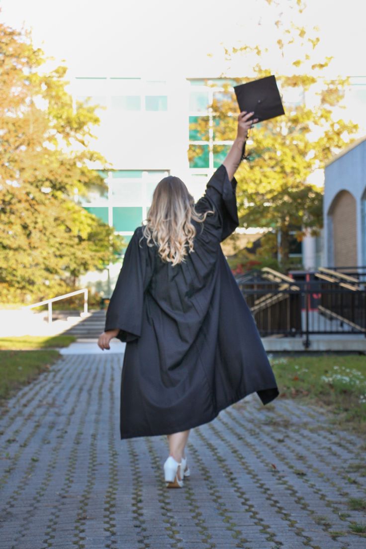 a woman in a graduation gown is walking down the street with her hands up and holding a book