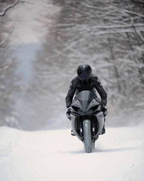 a man riding a motorcycle down a snow covered road in the middle of wintertime