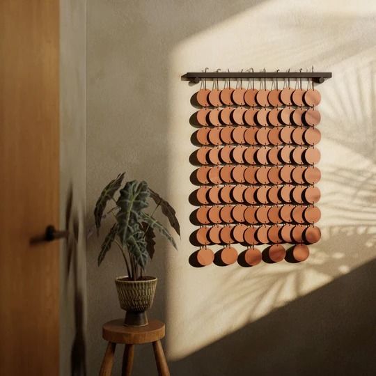 a plant is sitting on a stool in front of a wall hanging made out of clay circles