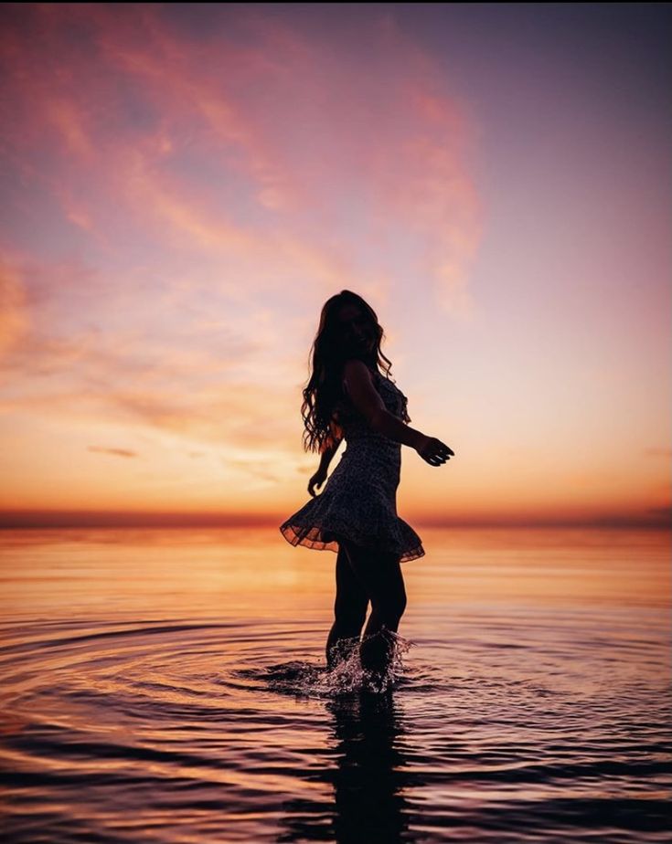 a girl standing in the water at sunset with her arms outstretched and head back to the camera