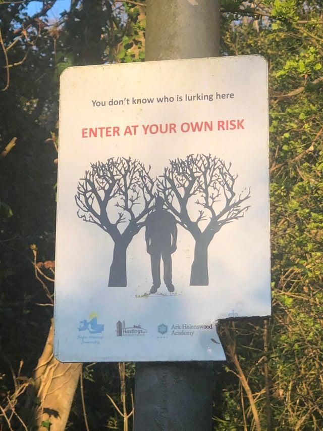 a sign posted on a pole in front of some trees with the words enter at your own risk