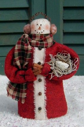 a snowman with a red coat and hat holding a bird's nest in his hand