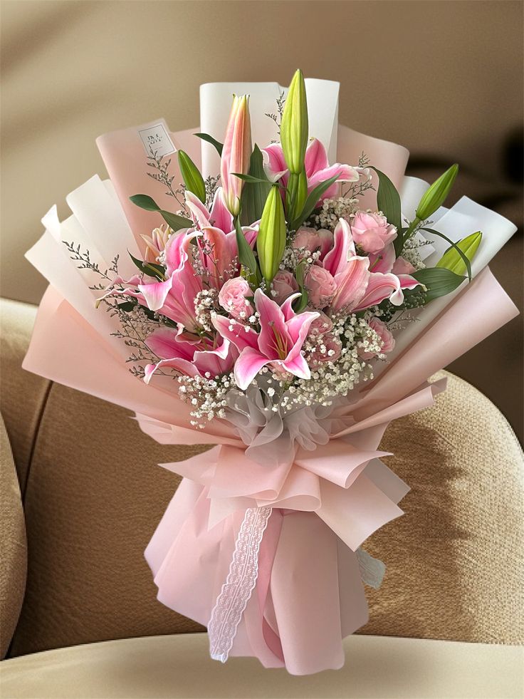 a bouquet of pink lilies and baby's breath wrapped in ribbon on a chair