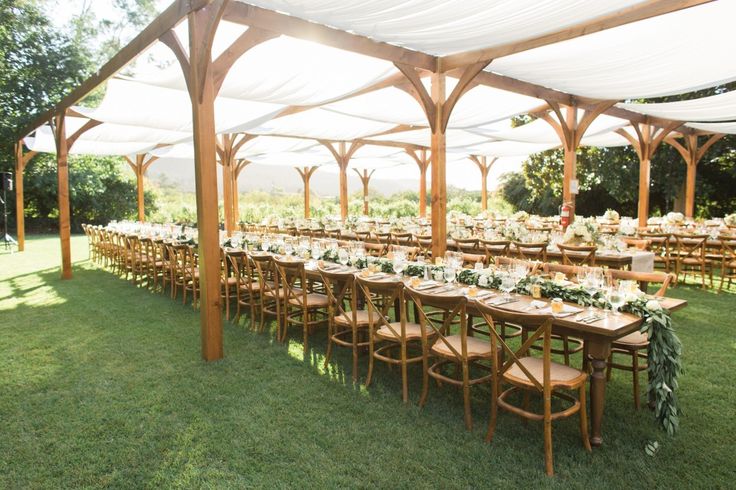 an outdoor wedding reception setup with wooden chairs and tables covered in white draping