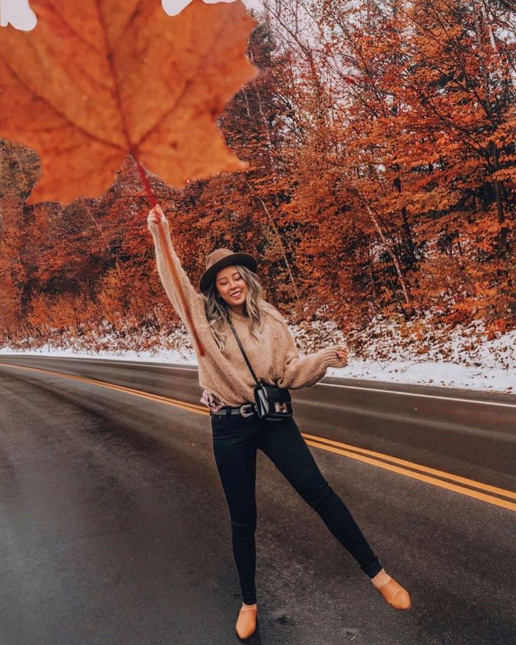 a woman standing on the side of a road holding an autumn leaf