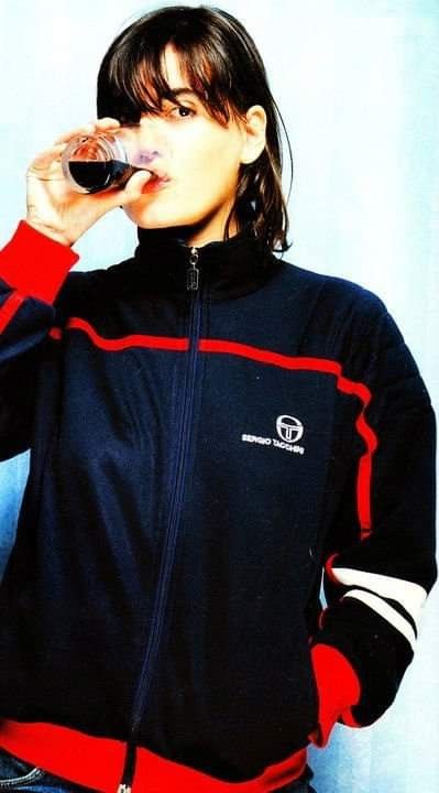 a woman drinking from a wine glass while wearing a black and red jacket with striped sleeves