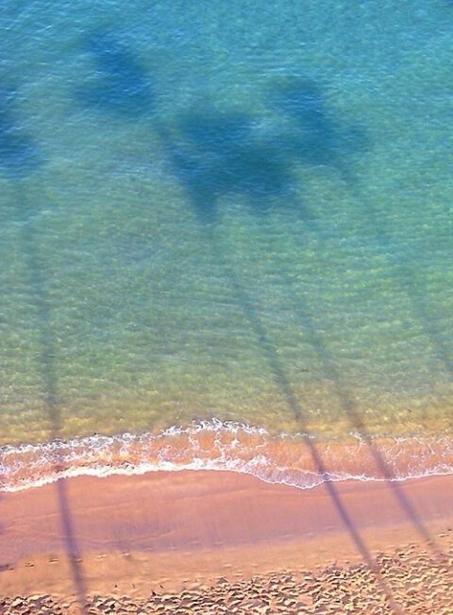 an aerial view of the ocean and beach from above, with shadows on the sand