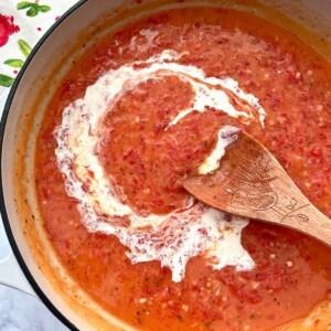 a wooden spoon in a pot filled with tomato sauce