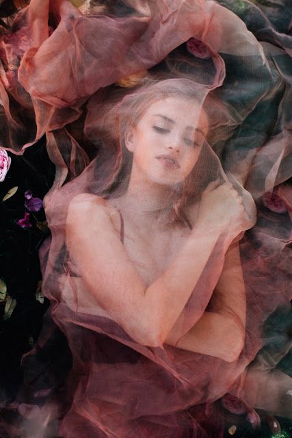 a woman with her eyes closed is covered by sheer fabric and flowers in the background