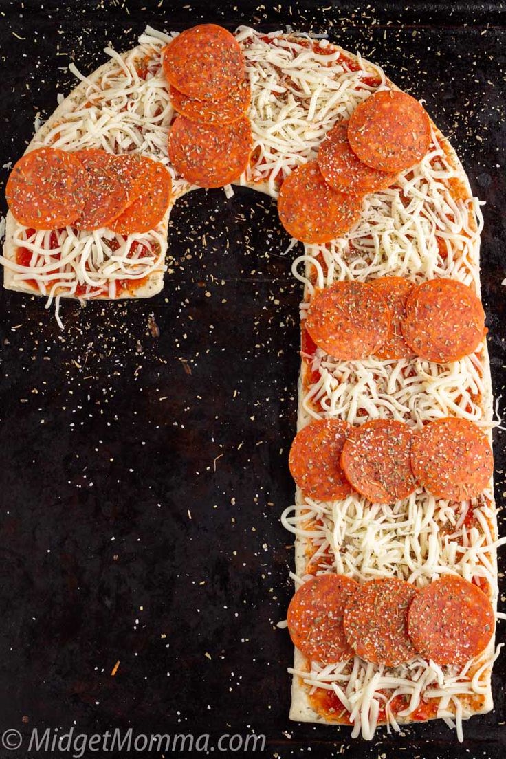 a pizza letter made out of cheese and pepperoni on a black surface with sprinkles