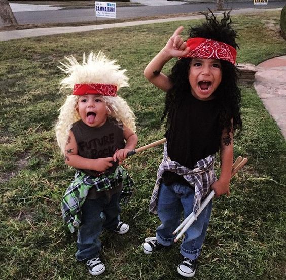 two young children dressed up in costumes on the grass with one holding a baseball bat