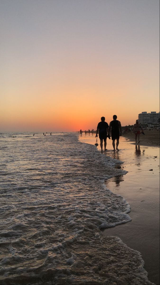 two people walking on the beach at sunset