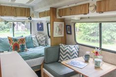 the interior of a camper with couches, tables and chairs in front of windows