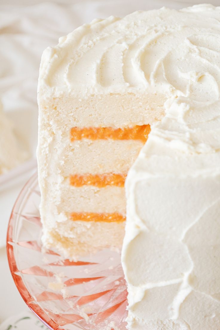 a cake with white frosting and orange stripes is cut from the side on a glass plate