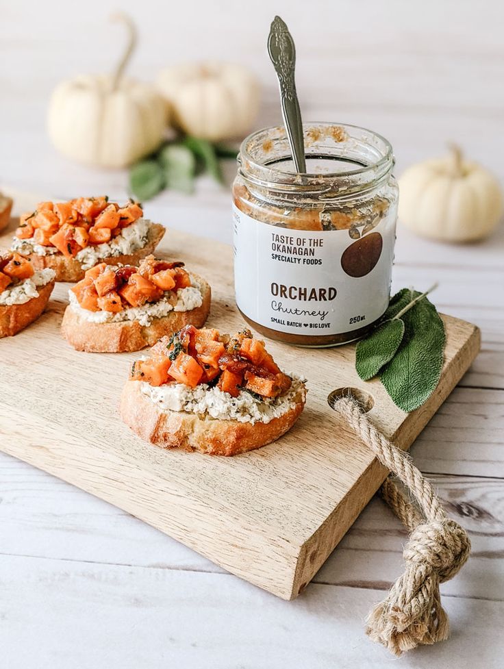 several small sandwiches on a wooden board with a jar of marmalade in the background