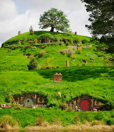 the hobbot house is surrounded by lush green grass and has trees on top