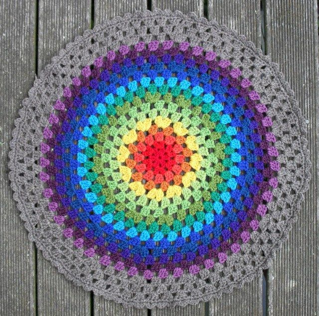 a multicolored crocheted doily sits on a wooden surface