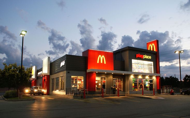 a mcdonald's restaurant at dusk with cars parked in the parking lot behind it