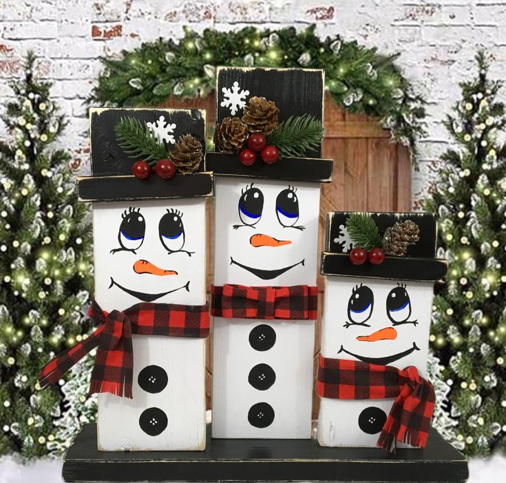 snowmen made out of wooden blocks sitting in front of a christmas wreath