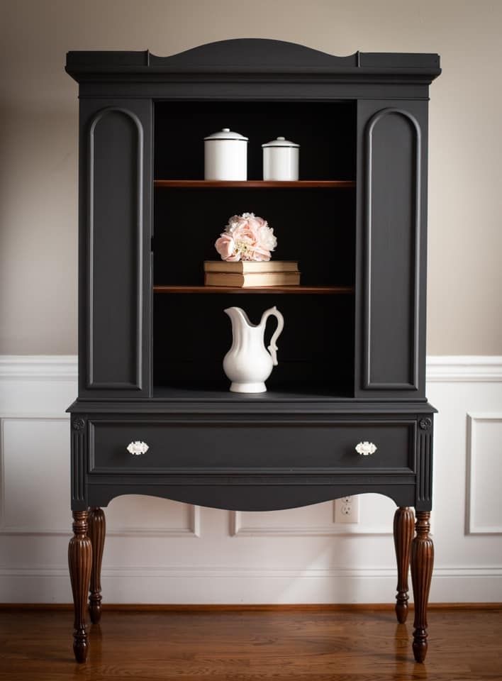 a black china cabinet with flowers on top and two vases in the bottom shelf