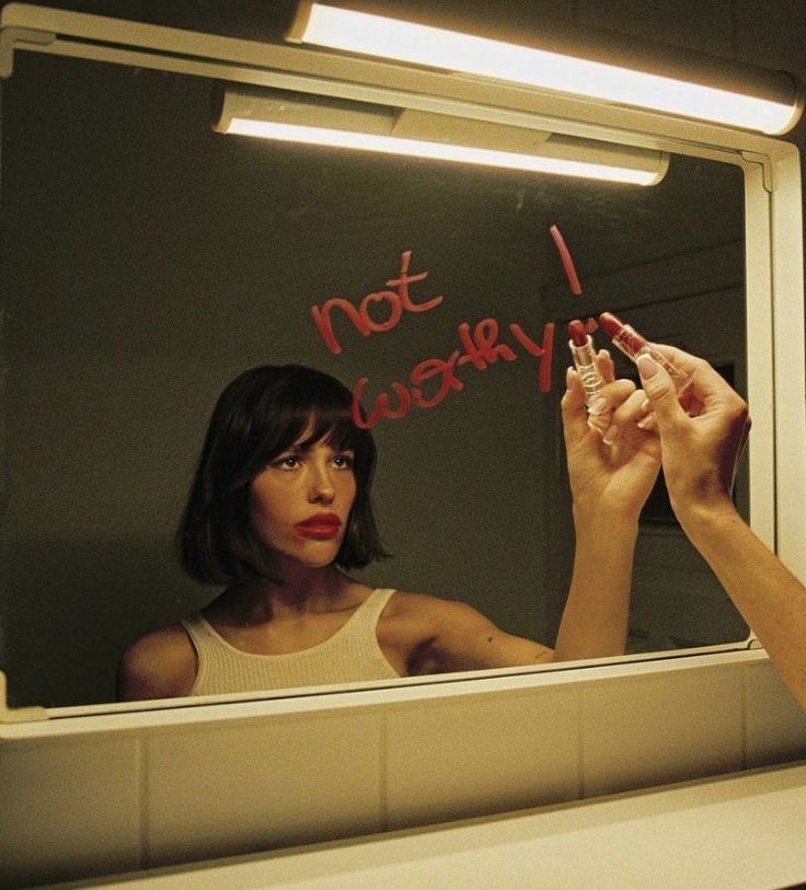 a woman is writing on the mirror with her hand and lipstick in front of her