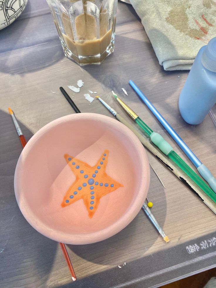 a pink bowl with an orange starfish painted on it next to paintbrushes