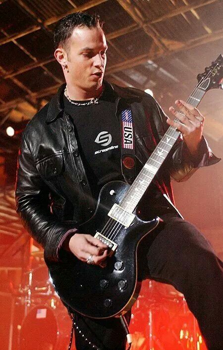 a man with a black guitar in his hand and wearing a leather jacket on stage