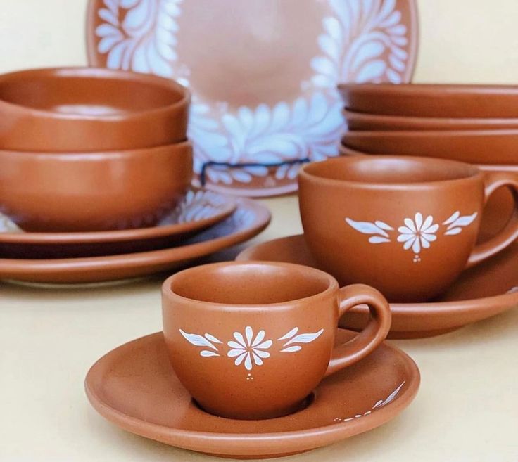 a set of brown cups and saucers with white flowers painted on the rims