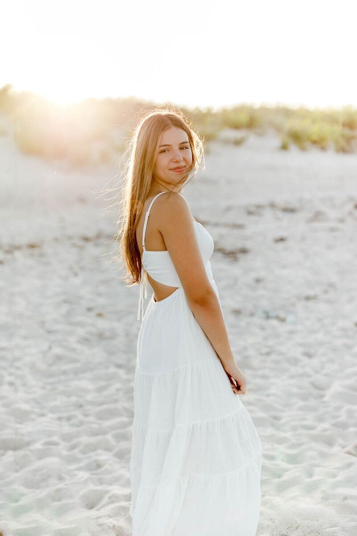 a woman standing on top of a sandy beach next to the ocean wearing a white dress