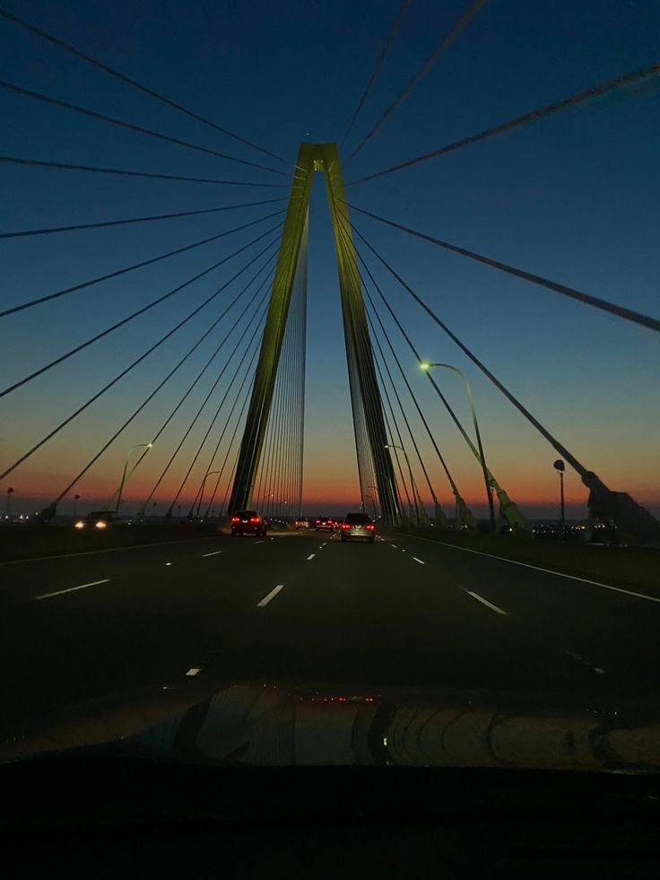 the sun is setting over a bridge with cars driving on it