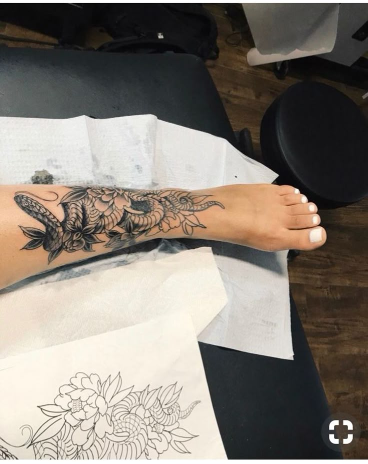 a woman's foot with tattoos on it sitting on top of a table next to papers