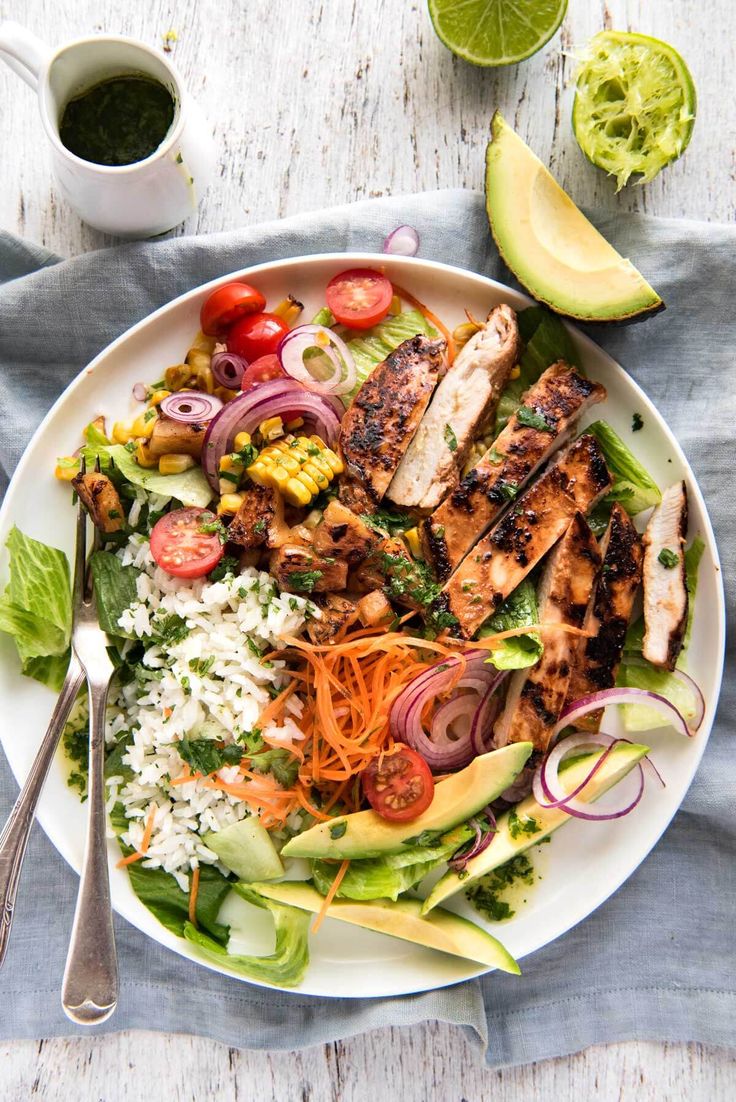 a white plate topped with chicken, rice and veggies next to an avocado