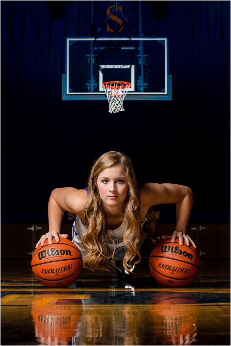 a beautiful young woman holding two basketballs on top of a court