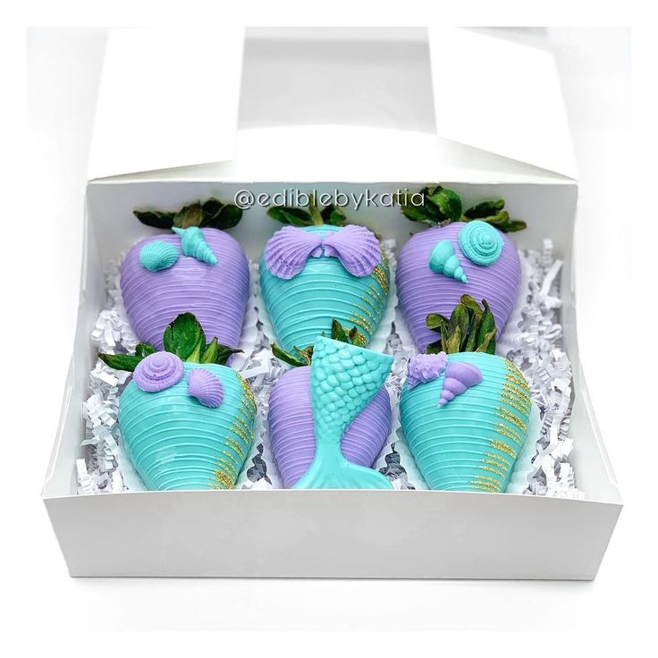 four blue and purple decorated strawberries in a white box