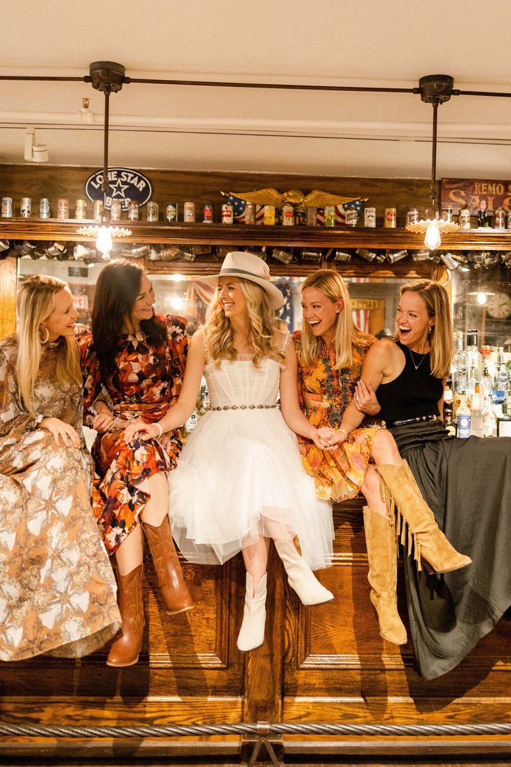 four women are sitting on a bar and having fun with each other in the background