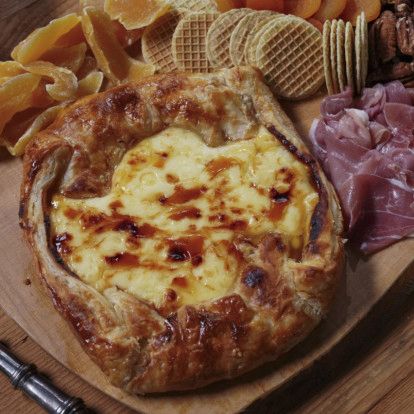 a wooden cutting board topped with cheese and meats next to crackers on top of it