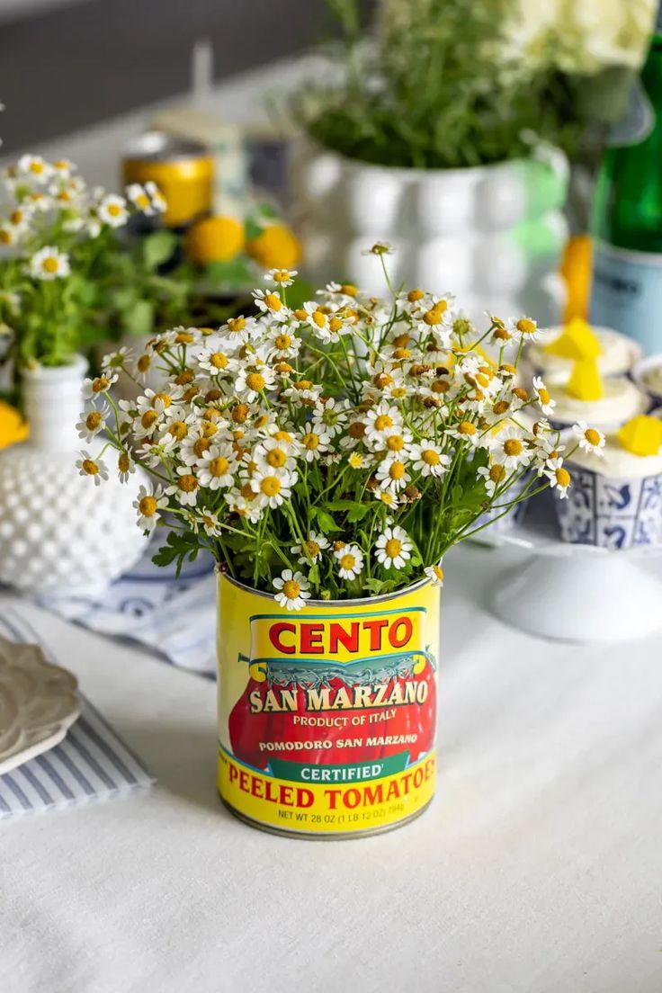 a can filled with daisies sitting on top of a table next to other flowers