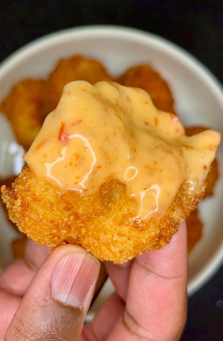 a person holding up a fried item with sauce on it