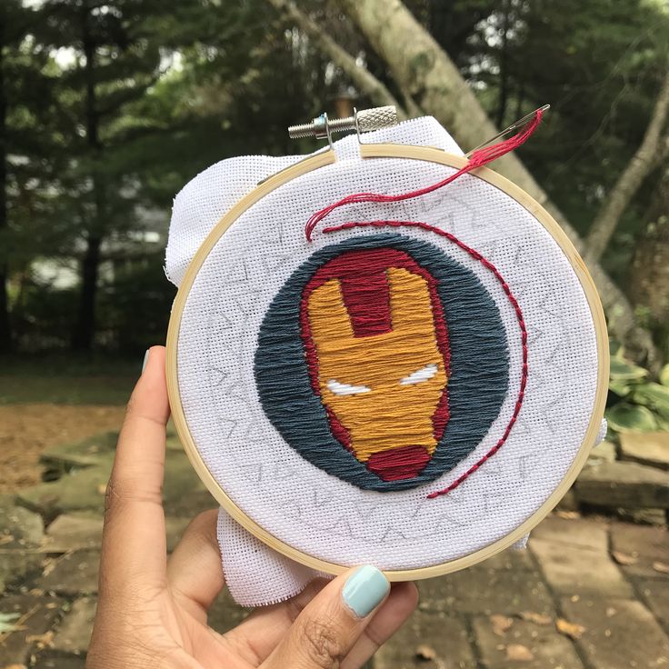 someone is holding up a iron man embroidered on a piece of fabric in front of some trees