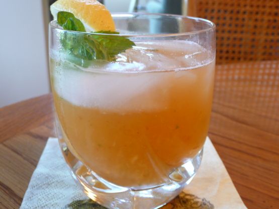 a glass filled with liquid sitting on top of a wooden table next to an orange slice