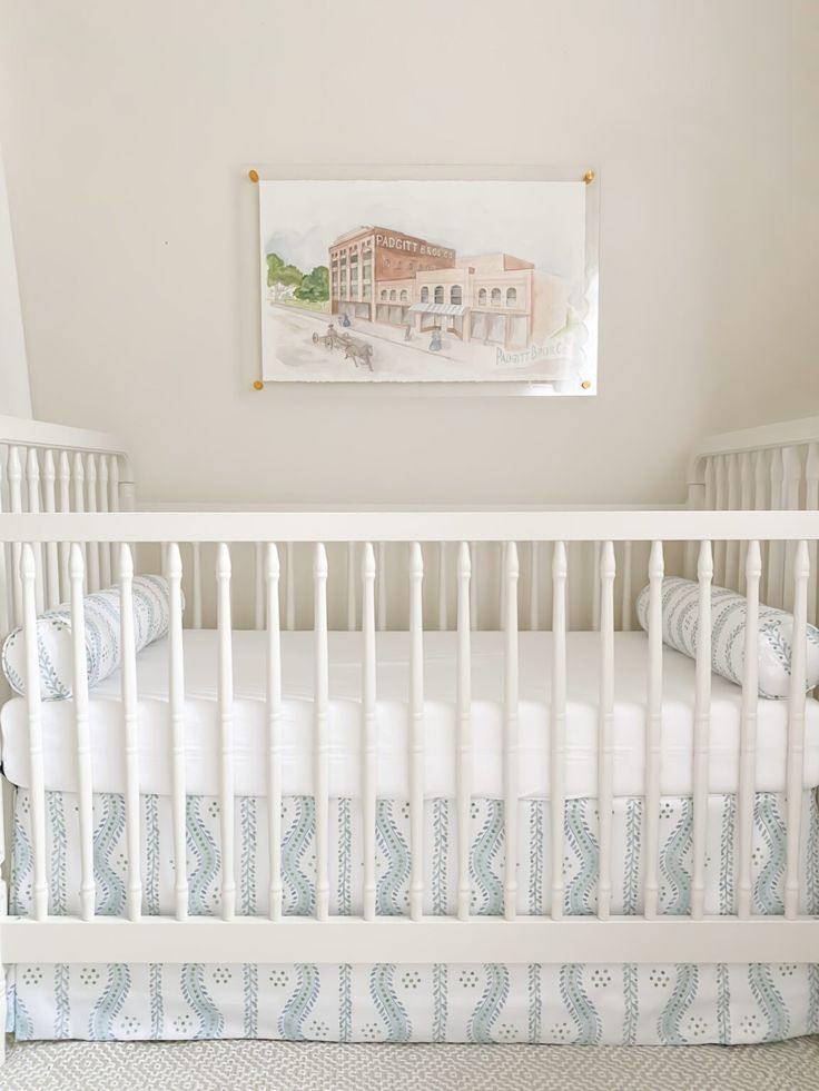 a white crib with blue and white bedding in a room that has a painting on the wall