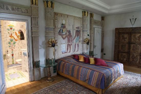 a bed sitting in a bedroom next to a tall wooden dresser and window with egyptian paintings on it