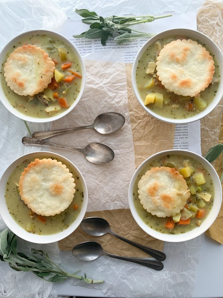 four bowls filled with soup next to silver spoons on top of a paper towel