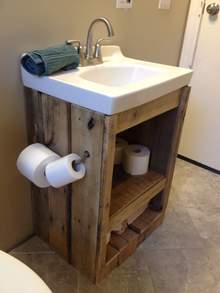 a bathroom sink made out of wood with two rolls of toilet paper on the shelf