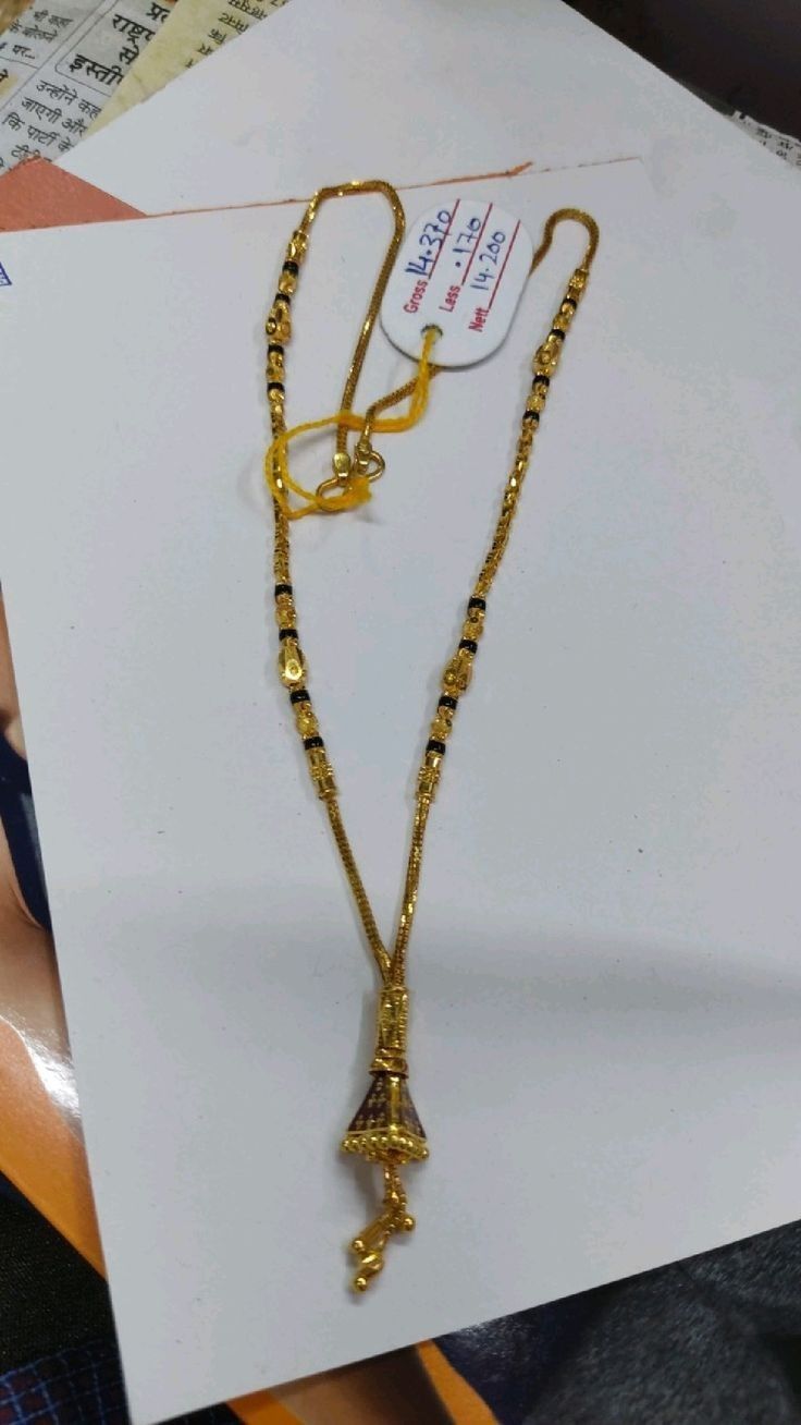 a gold necklace is displayed on top of a piece of paper with a tag attached to it