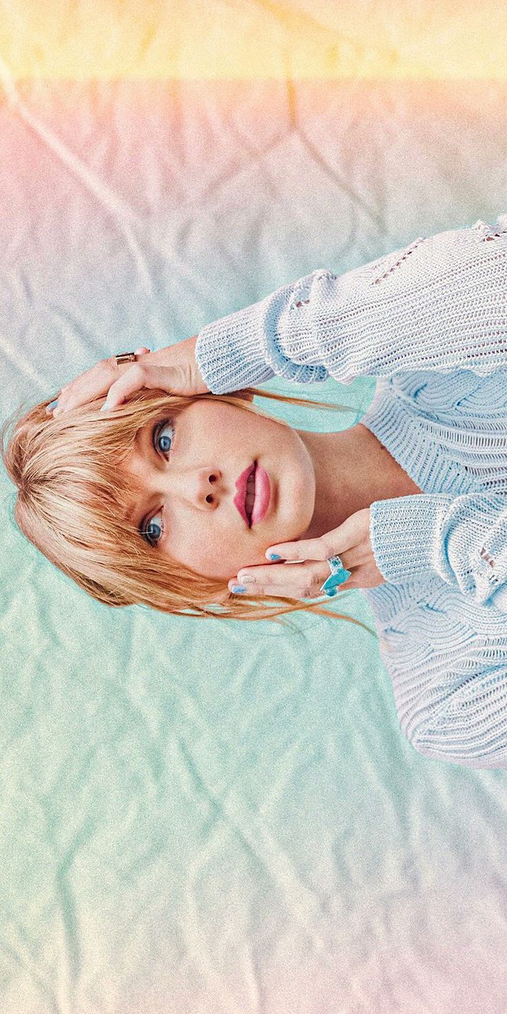 a woman with blonde hair and blue eyes poses for a photo in front of a pastel background