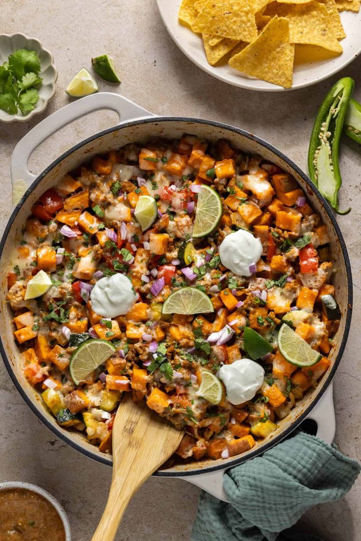 a skillet filled with mexican food next to tortilla chips and lime wedges