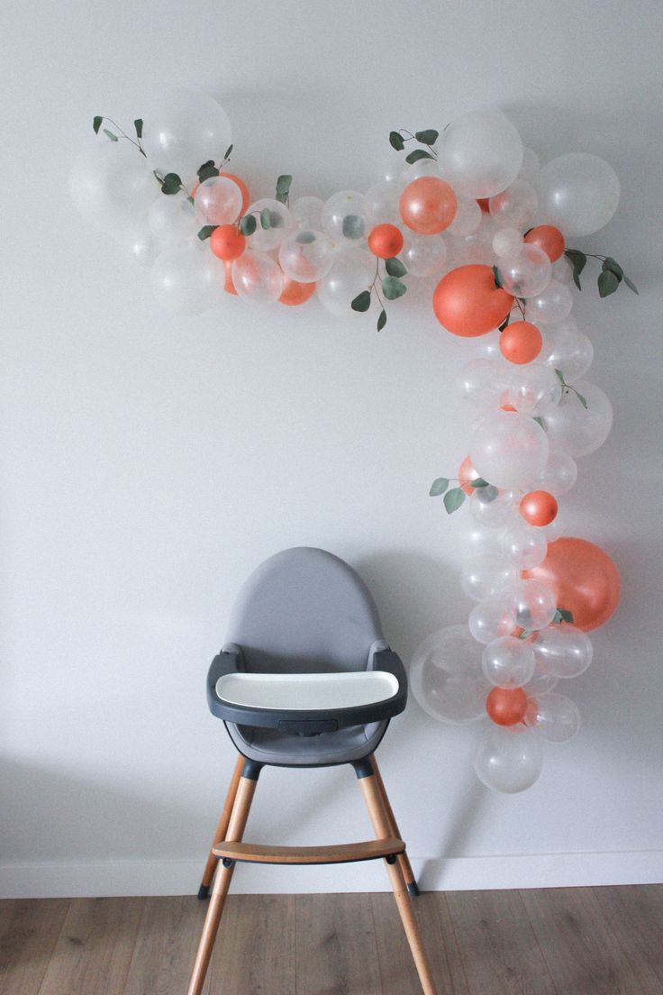 a baby's high chair in front of a balloon wall with orange and white balloons