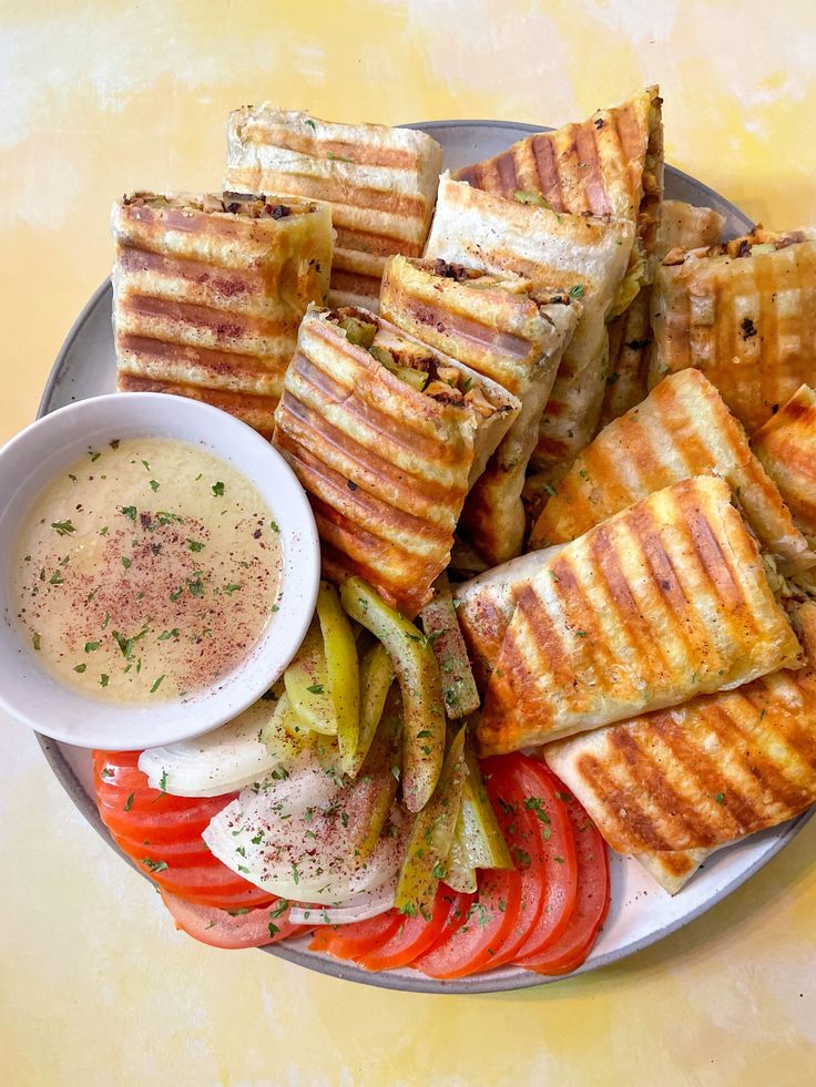 a plate filled with grilled sandwiches and veggies next to a bowl of dipping sauce