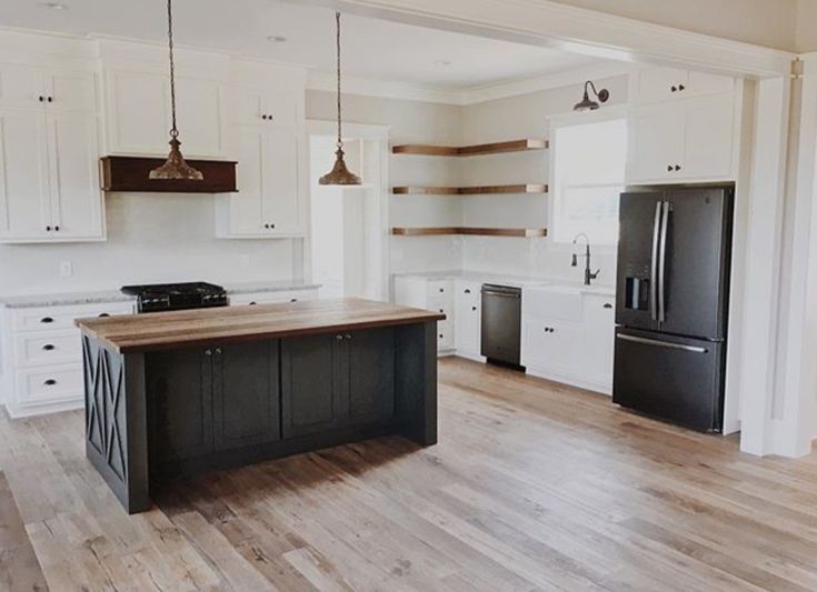 an empty kitchen with wood floors and white cabinets, black appliances and wooden flooring